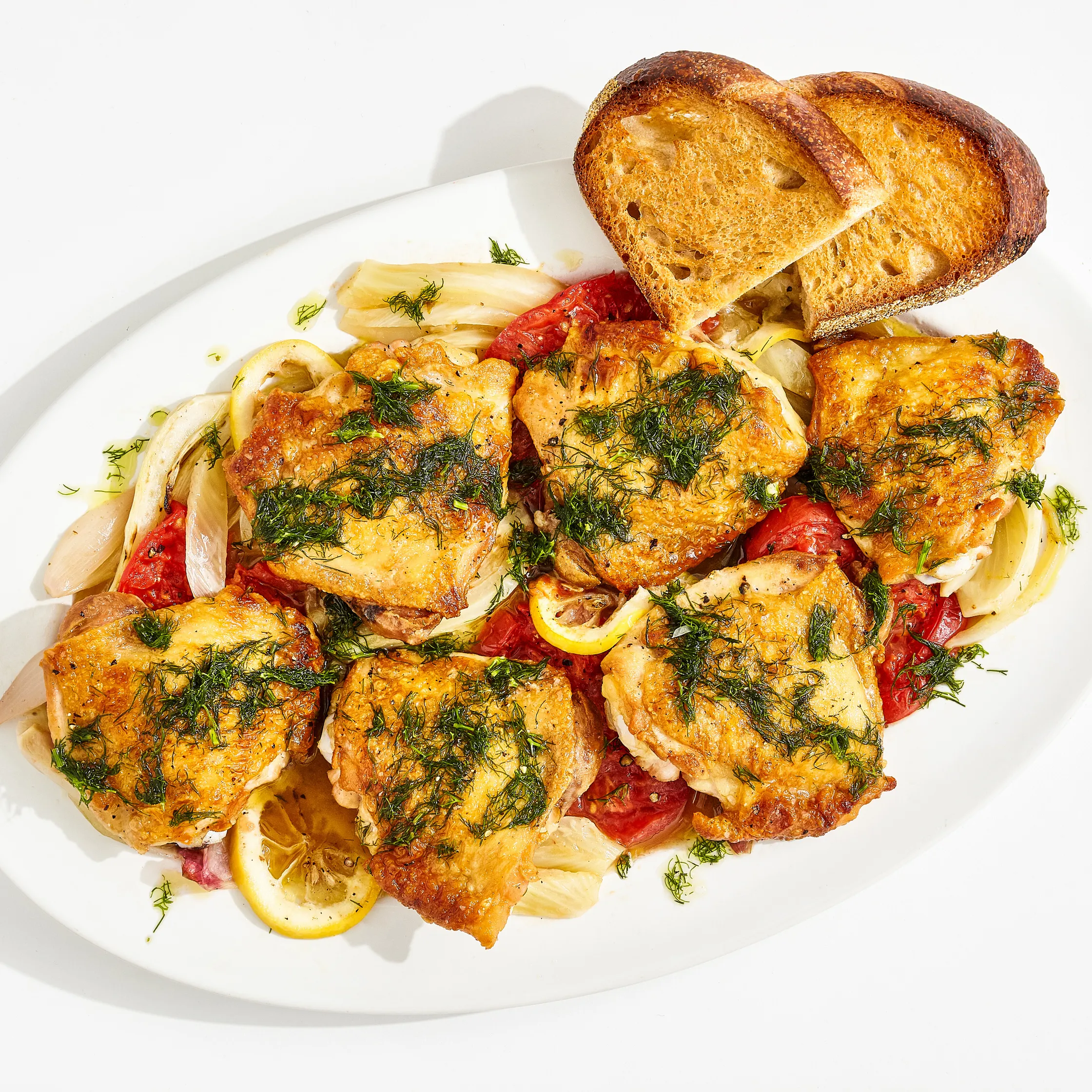 Roasted chicken thighs with caramelized fennel wedges, lemon rounds, and dill in a shallow serving dish